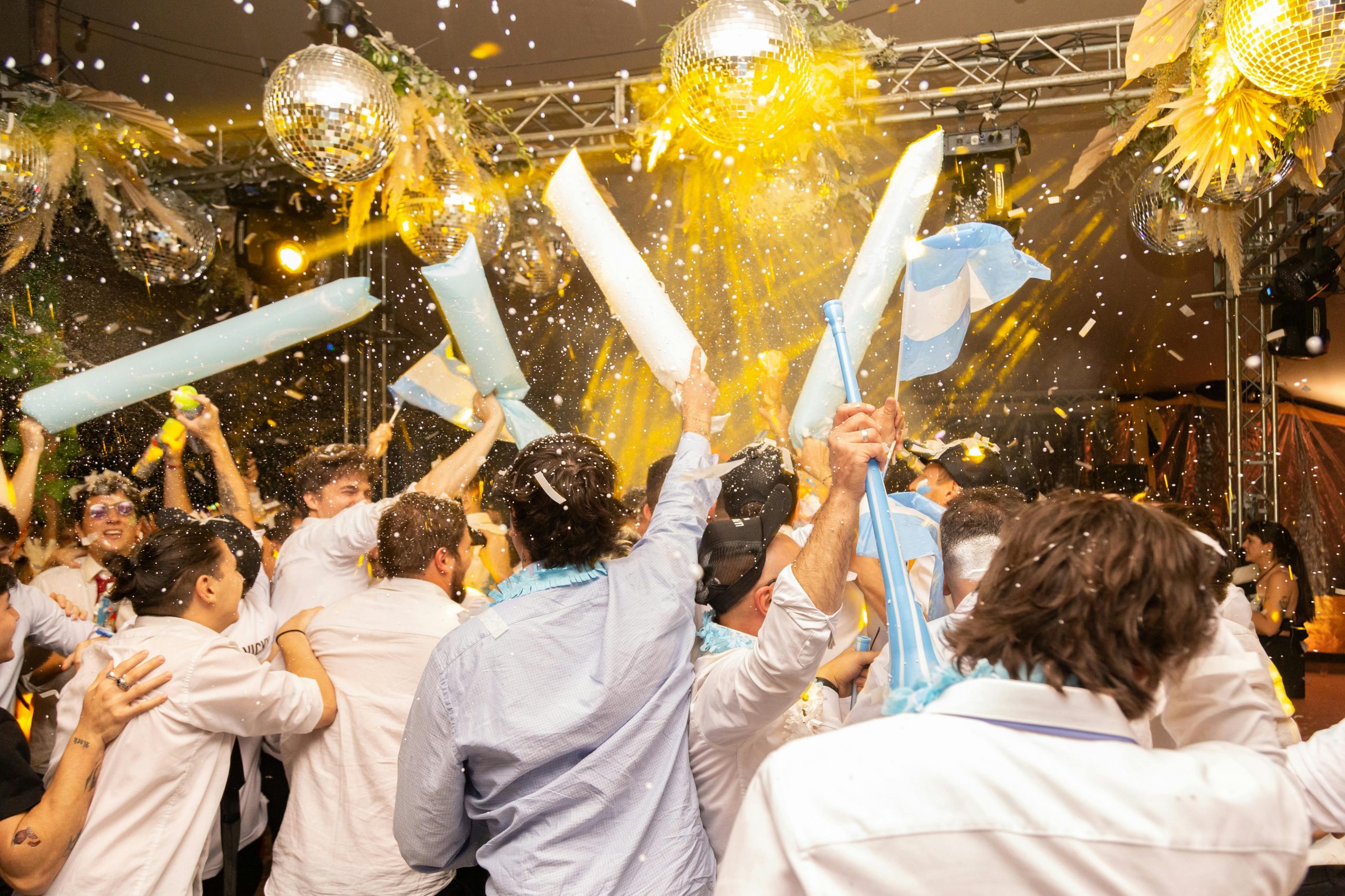 Joyous indoor party scene with people celebrating under disco balls and confetti in Mendoza, Argentina.